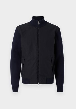 Navy and black jacket with a high collar, zip closure, and ribbed cuffs. Features side pockets and a mix of smooth and textured materials.