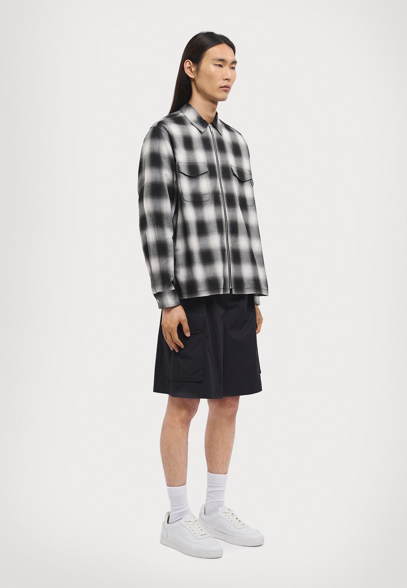 Black and white plaid flannel shirt with button-down collar, two chest pockets, paired with black cargo shorts and white sneakers.