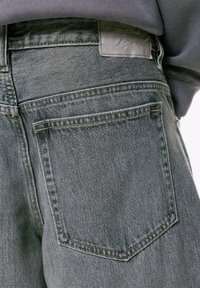 Nahaufnahme einer grauen Jeansrückentasche mit sichtbaren Nähten und einem verblassten Pull&Bear-Lederetikett am Bund.