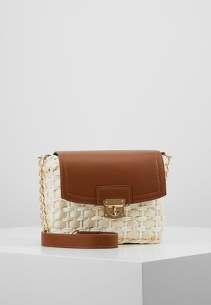 Geflochtene cremefarbene Handtasche mit braunem Lederklappe, goldener Verschluss und Kettenriemen, auf einem weißen Sockel vor einem hellgrauen Hintergrund liegend.