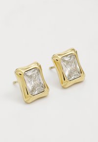 Boucles d'oreilles en métal doré ornées de pierres transparentes taillées en carré avec une surface facettée, encastrées dans un cabochon métallique ondulé de couleur dorée.