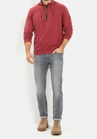 Pull-over en polaire rouge avec une demi-fermeture éclair, cordons marron, associé à un jean gris clair et des bottes beige. Coupe décontractée, poignets et ourlet côtelés.