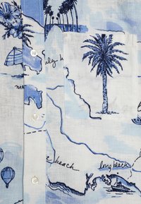 Camicia di lino azzurro chiaro con stampa di palme, bottoni e taschino con illustrazioni di spiagge e mongolfiere.