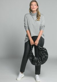 Grauer Rollkragenpullover, eng anliegende schwarze Hose und eine große, geraffte schwarze Handtasche. Weiße Sneakers mit einer dicken Sohle. Lässiges Outfit.
