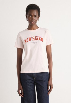 Lyserosa bomulls t-skjorte med en dristig rød buet tekstgrafikk "NEW HAVEN SPORTS CLUB". Korte ermer og rund hals.