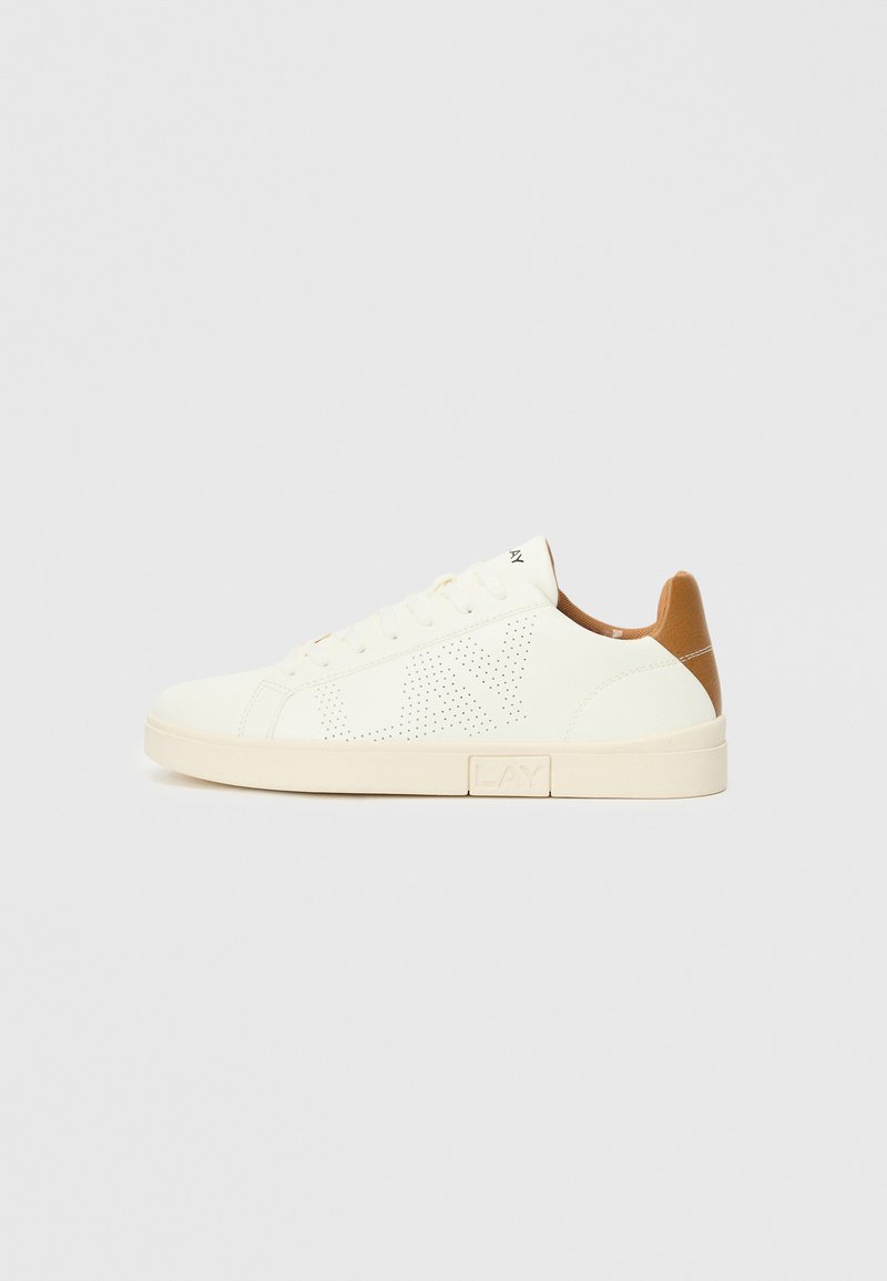Basket blanche avec des détails perforés, semelle beige clair et accents tan au niveau du talon. Design à lacets avec une texture lisse.