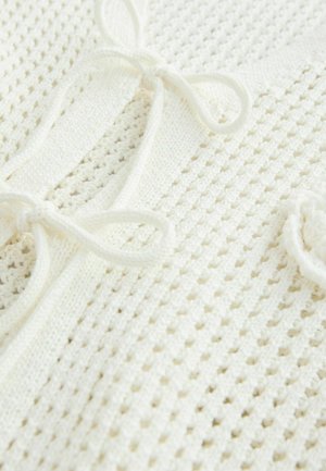 Top bianco lavorato a maglia con un motivo testurizzato, caratterizzato da lacci e un tessuto a trama aperta che migliora la traspirabilità. Tessuto morbido e leggero.
