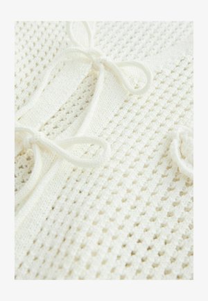 White knitted top with a textured pattern, featuring ties and an open weave that enhances breathability. Soft, lightweight fabric.