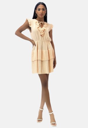 Vestido rizado de melocotón con mangas cortas, tejido texturizado, escote en v y falda de volantes. Llevado con tacones neutrales de tiras.
