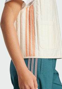 Beige quilted vest with orange accent stripes and a front pocket, paired with dark teal pants featuring striped details.