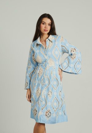 Robe bleu clair à manches longues, avec des découpes en dentelle complexes et des motifs en diamants. Conçue avec une taille ceinturée et un devant à boutons.