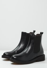 Botas Chelsea de cuero negro con paneles laterales elásticos, punta redondeada y suela de goma texturizada. Acabado suave y detalle de costura mínimo.