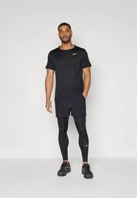 Conjunto atlético negro que incluye una camiseta de manga corta, pantalones cortos y leggings ajustados, todos con un logo blanco de Nike, complementados con zapatillas negras.