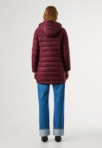 Bordo jakna s kapuljačom, s horizontalno četvrtastom teksturom, dugim rukavima i do koljena dugačkim dizajnom, u kombinaciji sa svijetloplavim trapericama.