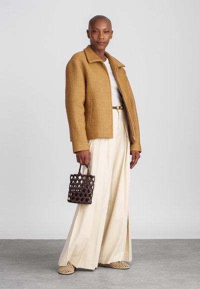 Brązowa żakiet w prążki, kremowy top, szerokie kremowe spodnie oraz pleciona brązowa torba. Lekko teksturowane materiały w luźnym kroju. Płaskie sandały.