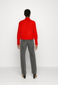 Rode, gebreide trui met een geribbelde textuur, cropped fit en hoge kraag, gecombineerd met grijze jeans met achterzakken en een rechte pijp.