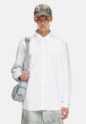 White shirt with light blue denim sleeves, buttoned up, paired with a striped strap bag and a camo cap. Casual, relaxed fit design.