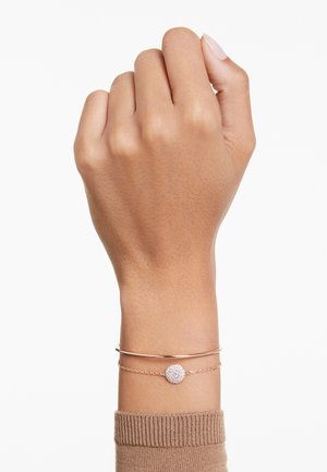 Bracciali in rosè su un polso; uno è un bracciale rigido liscio, l'altro presenta un ciondolo rotondo con pietre chiare e scintillanti. Il tono della pelle è medio.