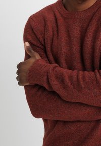 Maglione a maglia color ruggine con finitura testurizzata, scollo rotondo e maniche lunghe, con polsini a coste e una vestibilità comoda.