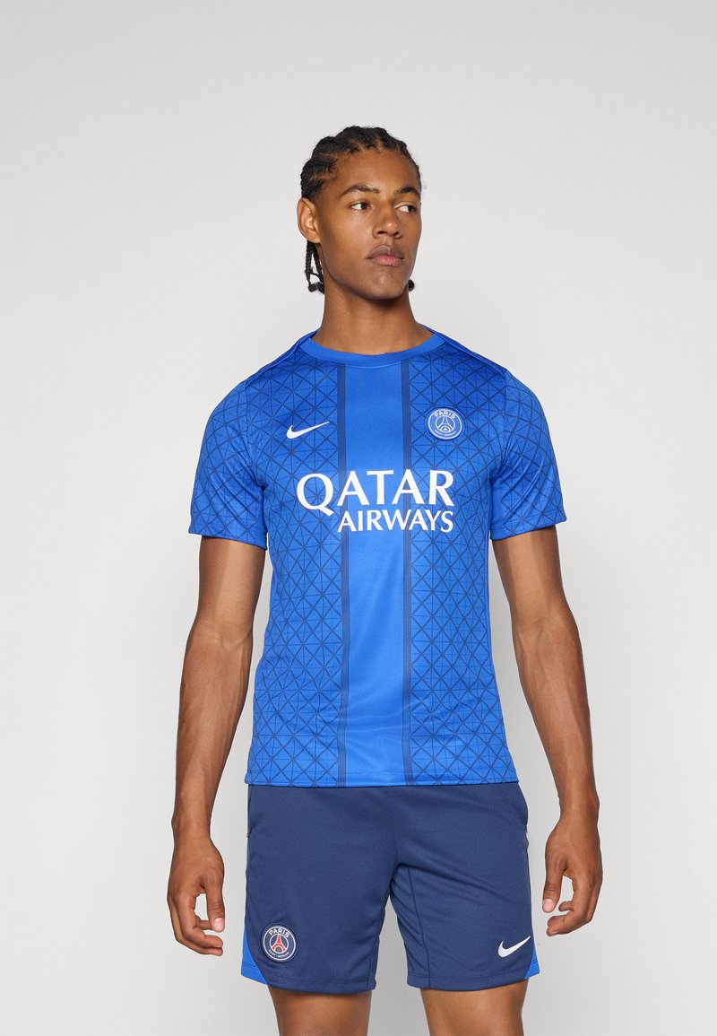Blå mønstrete fotballtrøye med korte ermer, med et geometrisk design og hvit "Qatar Airways"-logo. Bært med marineblå shorts.