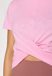 Κοντό ροζ T-shirt από απαλό, ελαφρύ ύφασμα με σχεδιασμό μπροστινού μέρους με γύρισμα, συνδυασμένο με καφέ κολάν ψηλόμεσο.