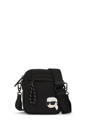 Black crossbody bag made of nylon. Features a smooth texture, zip closure, adjustable strap, and a cartoon patch on the front.