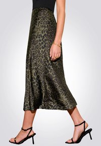 Jupe midi à imprimé léopard vert en tissu satiné, texture lisse, forme évasée, complétée par des sandales noires à lanières.