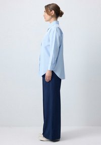 Camicia azzurra chiara con colletto a punta, maniche lunghe e orlo curvo. Abbinata a pantaloni navy a gamba larga e scarpe da ginnastica bianche.