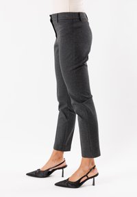 Pantaloni grigi su misura realizzati in tessuto strutturato, caratterizzati da una vestibilità slim, vita a media altezza e lunghezza cropped. Indossati con décolleté nere a punta.