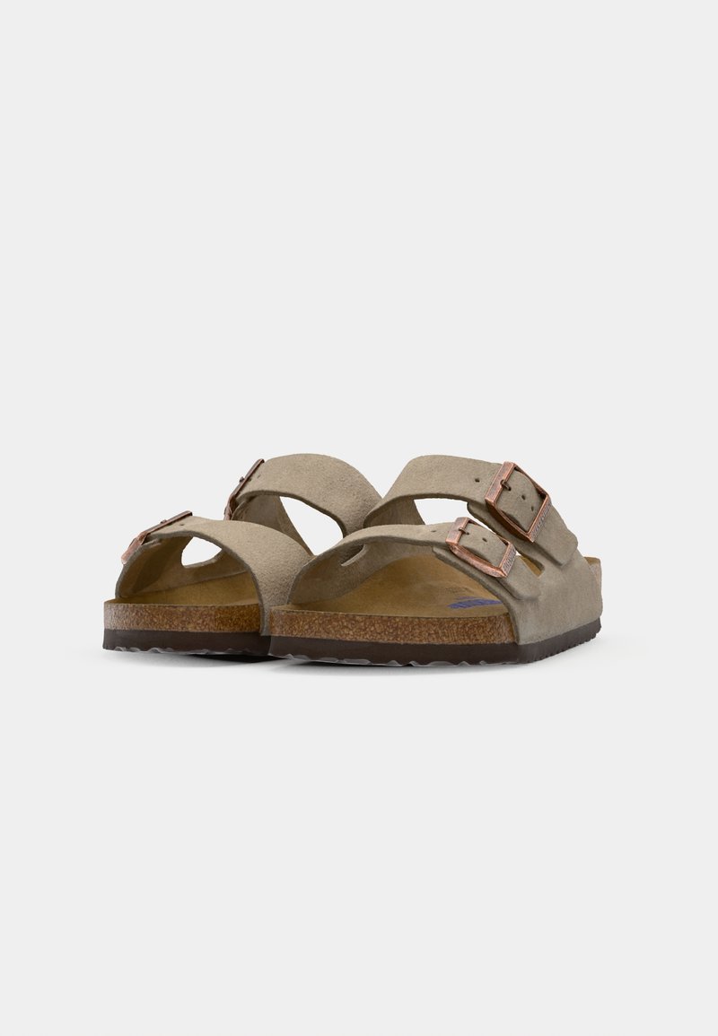 Two open-toed sandals in taupe suede with two adjustable straps and copper-colored buckles, featuring a cork footbed and textured rubber sole.