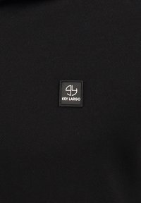 Tela negra con una pequeña etiqueta cuadrada negra que presenta un logo estilizado en blanco con las letras "gl" y el texto "KEY LARGO" debajo.