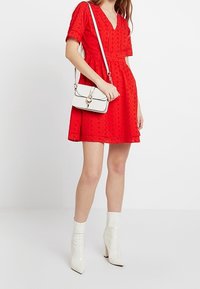 Robe rouge à manches courtes avec un décolleté en V et un motif floral texturé, associée à un sac à main blanc et des bottines blanches brillantes.