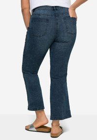 Jeans acampanados de mezclilla azul oscuro con bolsillos traseros, una cintura alta y dobladillos acampanados. Presentan una textura suave y detalles de costura mínimos.