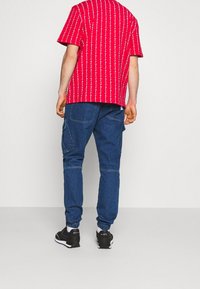 Camisa roja de manga corta con rayas verticales blancas, combinada con pantalones cargo azules con puños elásticos y bolsillos, usados con zapatillas negras.