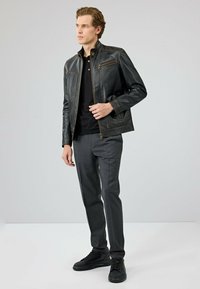 Zwarte leren jas met contrasterende stiksels, staande kraag, ritszakken, gecombineerd met grijze broeken en zwarte schoenen.