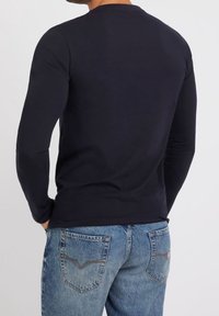 Mörkblå långärmad skjorta i bomull med rund hals. Bärs med blå denimjeans som har detaljer på bakfickorna.