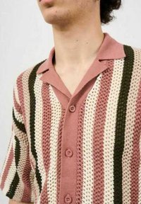 Camisa de punto de manga corta con un diseño de tejido abierto. Presenta rayas verticales en color rosa, crema y verde, un cuello con solapa y cinco botones.