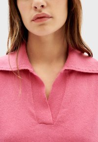 Roze gebreide pullover van een zachte, textuurstof met een kraag met inkeping en een diepe V-hals. Het kledingstuk heeft een relaxed fit.