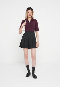 Burgundy lühikese varrukaga polo nööbitega, koos mustade volditud seelikutega. Mustad lamekontsad ja tumedad hallid põlvesokid täiendavad riietust.