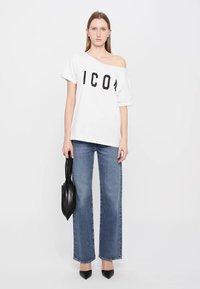 T-shirt blanc surdimensionné avec l'inscription "ICON" en noir, associé à un jean large bleu clair. Chaussures noires à bout pointu et un sac à main noir.