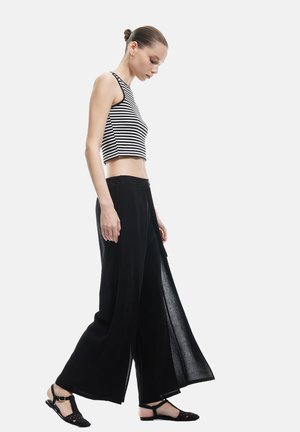 Sorte brede bukser parret med en sort-hvid stribet crop top. Letvægtsstof med en afslappet pasform og sideslids for nem bevægelse.