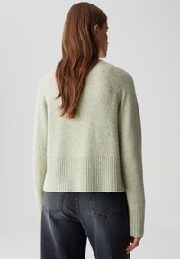 Mintgroene wollen trui met een geribde zoom en manchetten, uitgerust met een ontspannen pasvorm en een zachte textuur, gecombineerd met donkergrijze jeans.