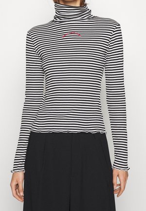 Lange mouwen turtleneck top met zwart-witte strepen, geribbelde textuur en een gegolfde zoom, met rode geborduurde tekst.