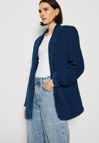 Merino corduroy takki rentoa leikkausta, kaulukset notched, pitkät hihat, yhdistettynä vaaleansinisiin farkkuihin ja valkoiseen puseroon.