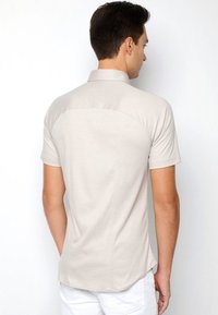 Beige polo shirt met korte mouwen en een kraag, met een gladde textuur en een gebogen schouderpas ontwerp aan de achterkant.