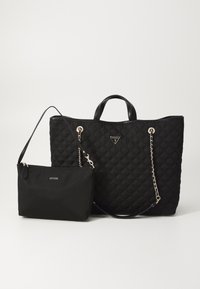 Sac cabas noir matelassé avec anses chaîne et petite pochette assortie zippée, toutes deux arborant le logo de la marque Guess.