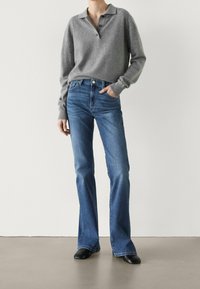 Grå stickad tröja med krage och tre knappar, ihop med blå utsvängda jeans. Slät tyg, klassisk design och figursydd midja.