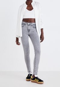 Grå denimjeans med en medelhög midja, i kombination med en vit crop-top och en oversized vit skjorta. Svarta sneakers med gula ränder.