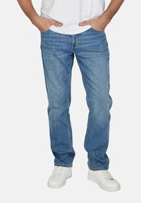 Jeans de denim de color azul claro con un corte recto, que cuentan con cinco bolsillos y un cierre de cremallera. Llevados con una camiseta blanca y zapatillas blancas.