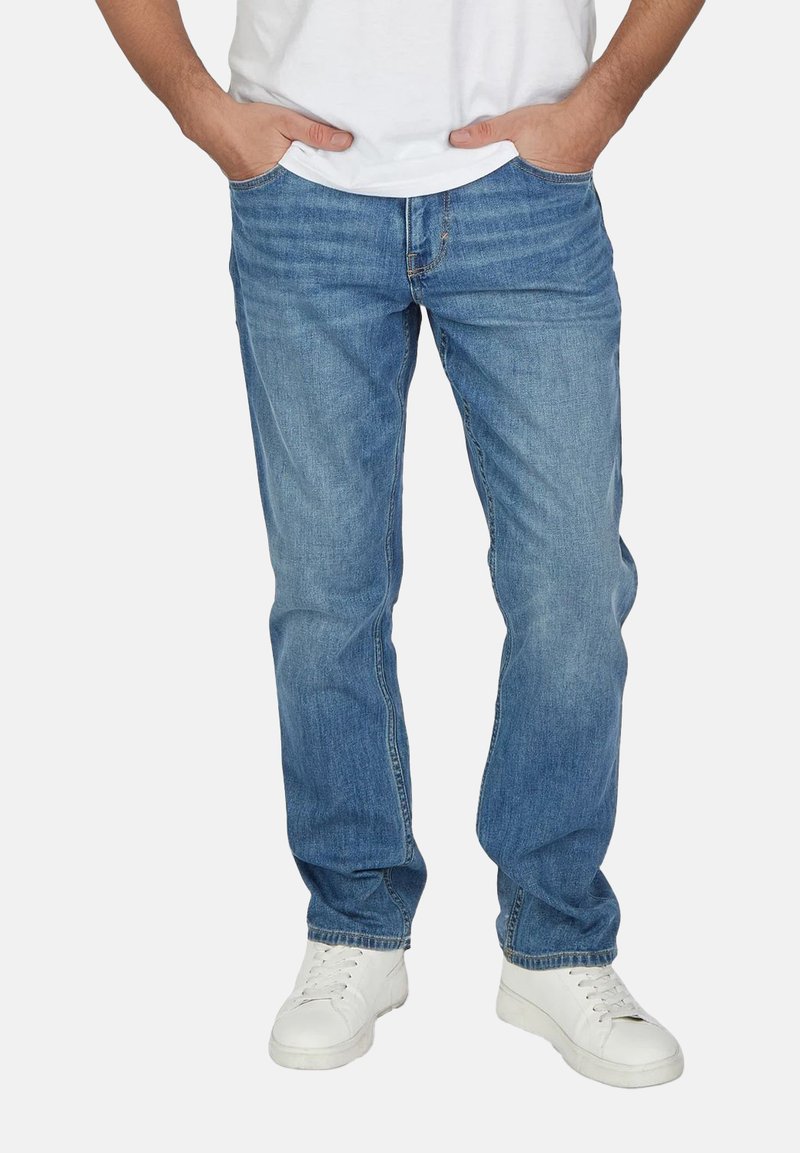 Jeans de denim de color azul claro con un corte recto, que cuentan con cinco bolsillos y un cierre de cremallera. Llevados con una camiseta blanca y zapatillas blancas.